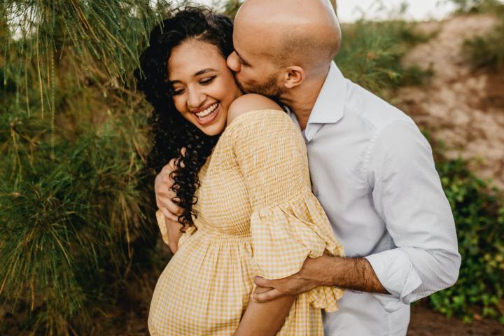 Pregnant couple embracing with man kissing cheek of woman